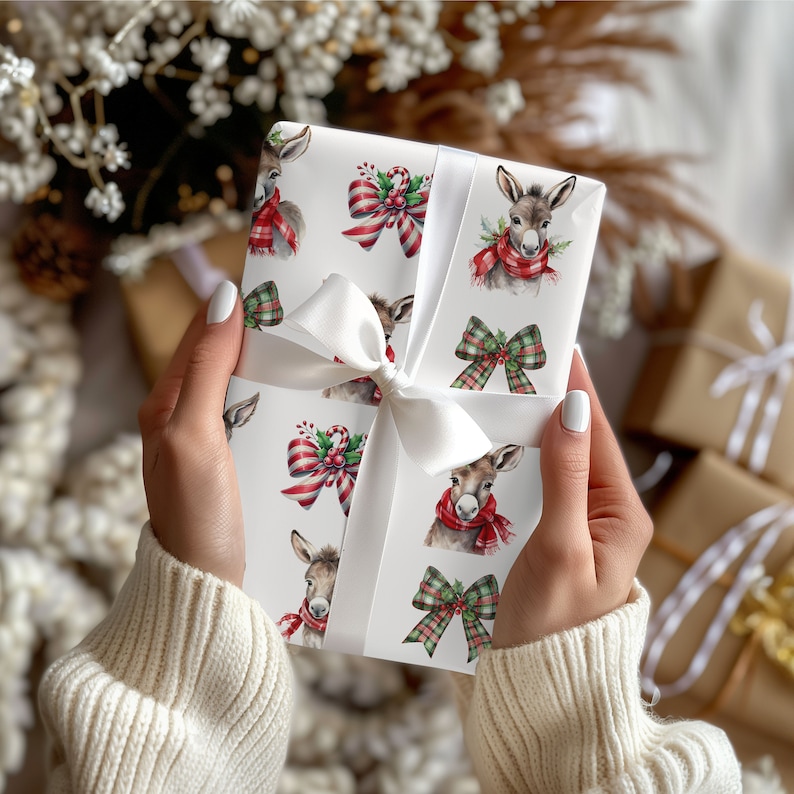 May include: A wrapped gift with white ribbon. The wrapping paper features a pattern of donkeys wearing red scarves, and red and green bows. The gift is held by a person wearing a cream-coloured sweater. Other gifts are in the background.