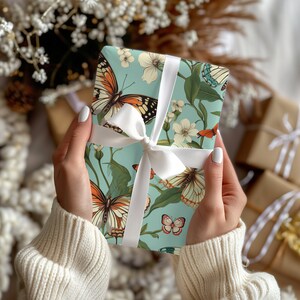 Puede incluir: Un papel de regalo azul claro con una cinta blanca y un patr&oacute;n de mariposas y flores. Las mariposas son en tonos de naranja, marr&oacute;n y blanco.