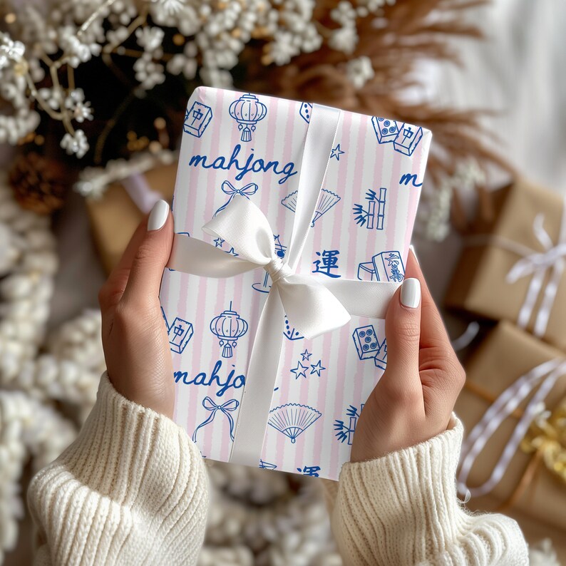 May include: A wrapped gift with pink and white striped paper featuring blue illustrations of lanterns, fans, and the word "mahjong." The gift is tied with a white satin ribbon and bow. Other wrapped gifts are in the background.