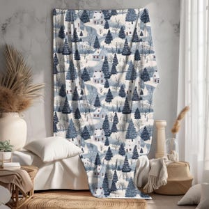 May include: A white and blue patterned throw blanket features a winter scene with houses and trees. The design is repeated throughout the blanket.