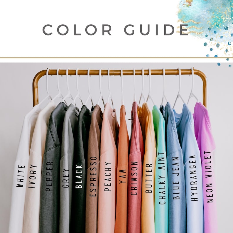 May include: A color guide featuring a variety of t-shirts in different colors, including white, ivory, pepper, grey, black, espresso, peachy, yam, crimson, butter, chalky mint, blue jean, hydrangea, and neon violet. The shirts are hanging on a gold rack.