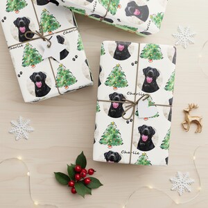 Pode incluir: Presentes embrulhados com papel branco com um padr&atilde;o repetido de Labrador preto, &aacute;rvores de Natal e pegadas. Cada pacote &eacute; amarrado com barbante e uma etiqueta em forma de cora&ccedil;&atilde;o. A palavra "Charlie" est&aacute; escrita.