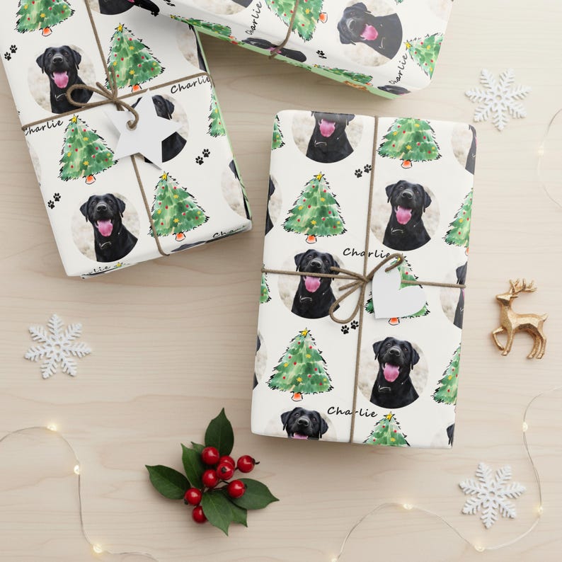 Pode incluir: Presentes embrulhados com papel branco com um padr&atilde;o repetido de Labrador preto, &aacute;rvores de Natal e pegadas. Cada pacote &eacute; amarrado com barbante e uma etiqueta em forma de cora&ccedil;&atilde;o. A palavra "Charlie" est&aacute; escrita.