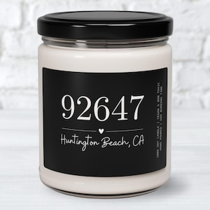 May include: A white candle with a black label that says "92647 Huntington Beach, CA". The candle is in a clear glass jar with a black lid.