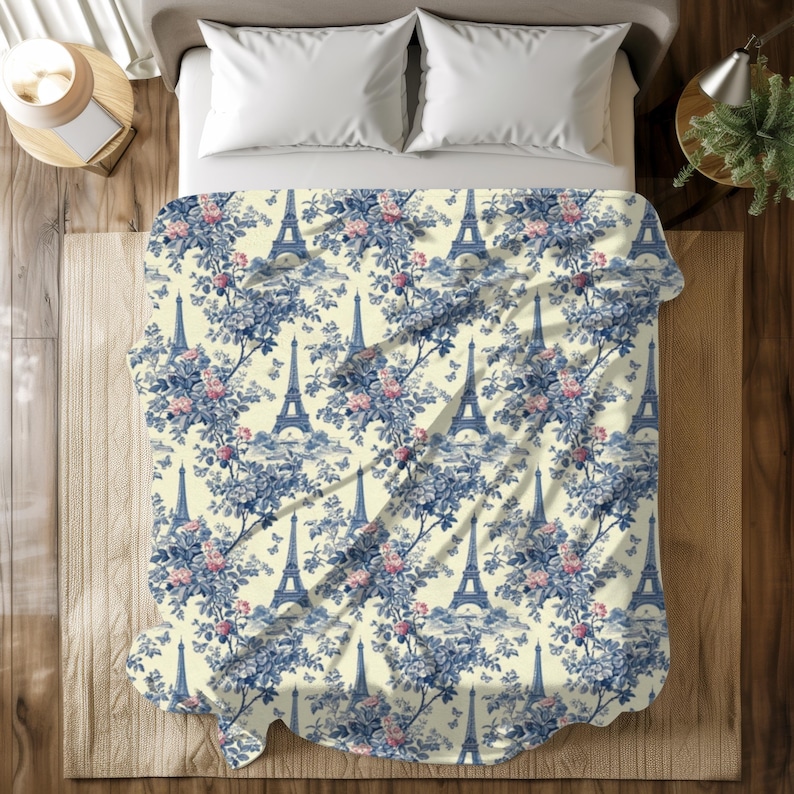 May include: A white and blue patterned throw blanket featuring a repeating design of the Eiffel Tower and floral bouquets. The blanket is made of soft, plush fabric and is perfect for adding a touch of Parisian charm to any room.