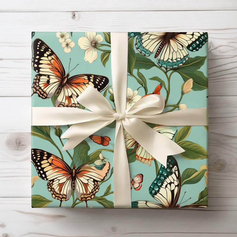 Puede incluir: Una caja de regalo envuelta en papel azul con una cinta blanca y un patr&oacute;n de mariposas y flores. Las mariposas son de color naranja, marr&oacute;n y negro con detalles blancos. Las flores son blancas con hojas verdes.