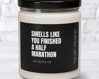 May include: A white candle in a glass jar with a black label that reads "Smells like you finished a half marathon" and "Dandy Nomads". The label also includes the text "100% Soy Candle | Vegan & Non Toxic | Hand Poured | 60h Burning Time".