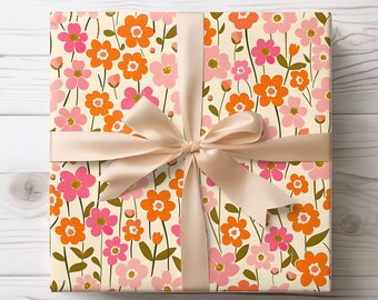 May include: A gift box wrapped in white paper with a floral pattern. The paper features pink and orange flowers with green stems. The box is tied with a beige satin ribbon.