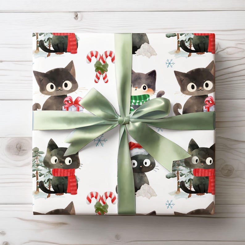 Puede incluir: Un regalo envuelto con papel blanco con un estampado de gatos negros con bufandas y gorros de Pap&aacute; Noel, bastones de caramelo y copos de nieve. Est&aacute; atado con una cinta y un lazo de raso verde salvia.