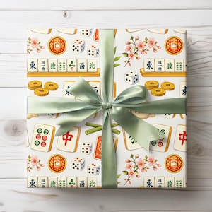 May include: A wrapped gift with a white background featuring a pattern of Mahjong tiles, dice, coins, and cherry blossoms. A light green satin ribbon and bow are tied around the gift. The Mahjong tiles have Chinese characters.