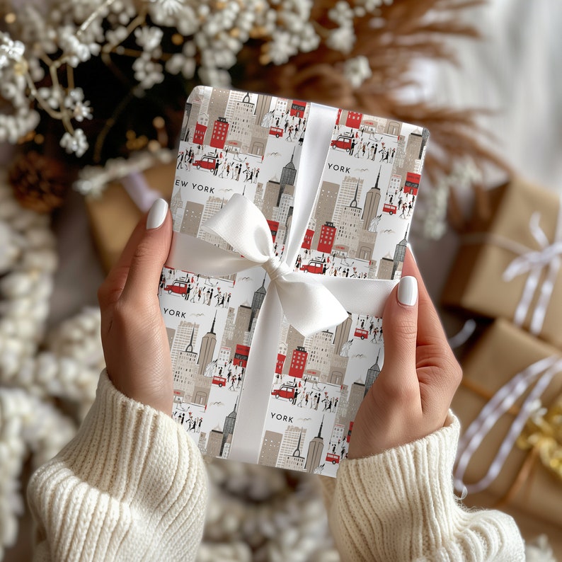 May include: White gift wrap with a repeating pattern of red and black New York City skyline illustrations. The wrapping paper is tied with a white satin ribbon.