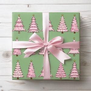 May include: A wrapped gift with green wrapping paper featuring a repeating pattern of pink Christmas trees with yellow star toppers. A light pink satin ribbon is tied in a bow around the gift.