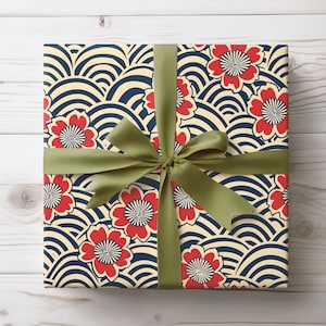 Puede incluir: Un regalo envuelto en papel con un estampado de flores rojas y dise&ntilde;os de olas azul marino sobre un fondo crema. Est&aacute; atado con una cinta y lazo de sat&eacute;n verde, ideal para ocasiones especiales.