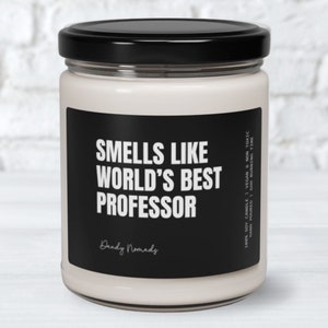 May include: A white soy candle in a glass jar with a black label that reads "Smells Like World's Best Professor" and "Dandy Nomads". The label also includes the details "100% Soy Candle | Vegan & Non Toxic | Hand Poured | 60h Burning Time".