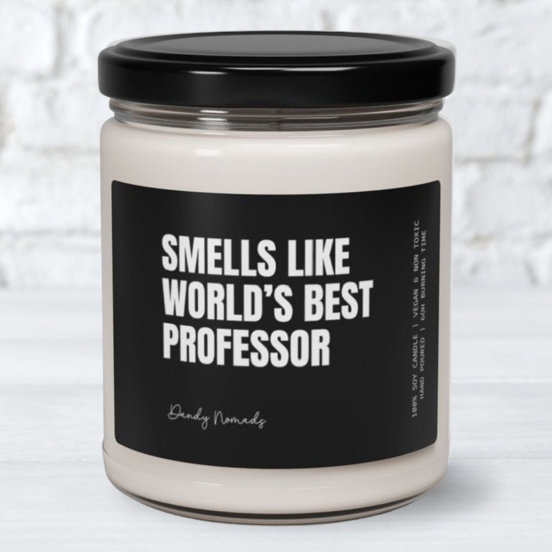 May include: A white soy candle in a glass jar with a black label that reads "Smells Like World's Best Professor" and "Dandy Nomads". The label also includes the details "100% Soy Candle | Vegan & Non Toxic | Hand Poured | 60h Burning Time".
