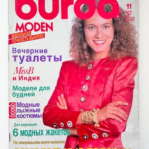 Può includere: Una copertina di rivista con una donna che indossa una giacca rossa con bottoni dorati e braccialetti. La rivista si chiama "Burda MODEN" e il testo "Abiti da sera" e "Miss B e India" è visibile. La copertina della rivista presenta anche il testo "Modelli per tutti i giorni" e "Tute da sci alla moda".