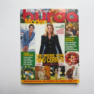 Op de afbeelding: Een vintage mode magazine met de titel "Moden" in grote rode letters. De cover bevat afbeeldingen van modellen, tekst waaronder "Kim Basinger" en "Nino Cerruti", en de zin "Bald ist Ostern".
