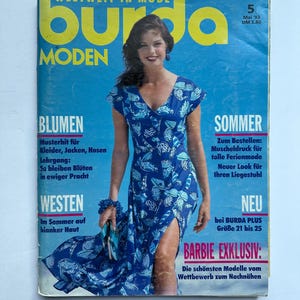 Op de afbeelding: Een tijdschriftomslag met een vrouw in een blauwe jurk met patroon. De titel "burda MODEN" is geel. Tekst bevat "BLUMEN" en "SOMMER". De omslag heeft een blauwe achtergrond. Tijdschrift uit mei '93.