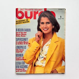 Puede incluir: Una portada de revista vintage con una mujer con un blazer amarillo y falda a juego. El título de la revista es "bur" en letras rojas grandes. El texto incluye "IN NEUEN FARBEN" y "Januar '92". La mujer sonríe y lleva pendientes dorados.