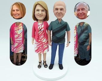 Puede incluir: Una pareja de figuritas personalizadas, la mujer lleva un vestido estampado en rosa y blanco y una chaqueta roja, y el hombre lleva una camisa a rayas verdes y negras y unos vaqueros azules.