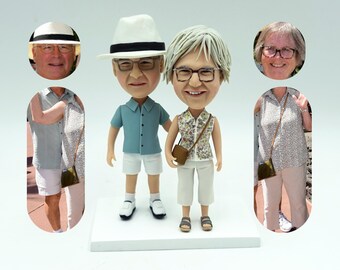 Puede incluir: Un conjunto de figuras personalizadas de una pareja, con el hombre vistiendo un sombrero blanco y una camisa azul y la mujer vistiendo una camisa floral y pantalones blancos. Las figuras están de pie sobre una base blanca.