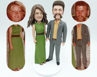 Puede incluir: Un adorno para pastel personalizado que representa a una pareja en estilo vintage. La mujer lleva un vestido verde y el hombre lleva un traje gris. La pareja está de pie sobre una base blanca.