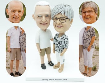 Puede incluir: Una pareja de figuritas personalizadas, un hombre y una mujer, con un fondo blanco. La pareja de figuritas está de pie uno al lado del otro. El hombre lleva una camisa blanca y pantalones cortos de color caqui. La mujer lleva una camisa con estampado gris y blanco y pantalones blancos. El texto "Happy 40th Anniversary" está impreso en la base de la figurita.