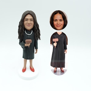 May include: A custom-made figurine of a person wearing a black judge's robe and holding a gavel. The figurine has a realistic face and is standing on a white base.