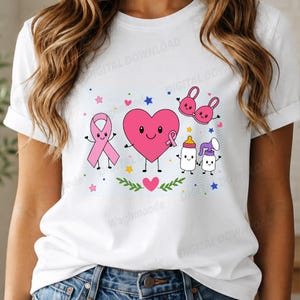 Könnte beinhalten: Ein weißes T-Shirt mit einem Grafikdruck, der ein rosa Herz, eine rosa Schleife, ein Babyfläschchen, eine Milchpumpe und einen rosa BH mit jeweils lächelnden Gesichtern zeigt, umgeben von kleinen bunten Sternen und einem grünen Blattzweig.