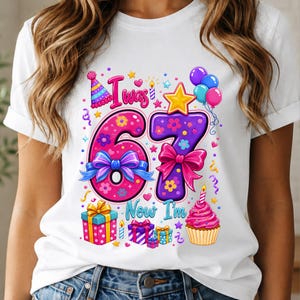 Könnte beinhalten: Ein weißes Kurzarm-T-Shirt mit einer bunten Geburtstagsgrafik. Das Design enthält den Text "I was 67 Now I'm" mit großen, mit Blumen und Schleifen verzierten Zahlen, umgeben von Luftballons, Geschenkkartons, einem Cupcake und einem Partyhut.