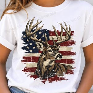 Könnte beinhalten: Ein weißes Kurzarm-T-Shirt mit einem Grafikdruck eines braunen Hirsches mit großem Geweih, zentriert über einem abgenutzten Design der amerikanischen Flagge. Die Flagge zeigt die Farben Rot, Weiß und Blau mit Sternen und Streifen.