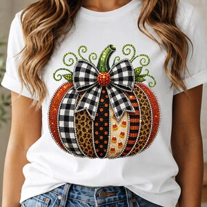 Könnte beinhalten: Ein weißes T-Shirt mit einer großen, zentralen Grafik eines mit Strasssteinen verzierten Kürbisses. Das Kürbisdesign umfasst Abschnitte mit schwarz-weißem Karomuster, Leopardenmuster, orangefarbenen Punkten, Zuckermais und Streifen.