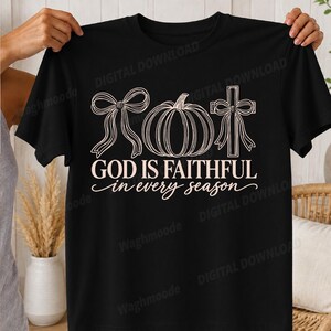 Könnte beinhalten: Ein schwarzes T-Shirt mit kurzen Ärmeln und einem hellrosa Grafikdesign. Der Aufdruck zeigt eine Schleife, einen Kürbis und ein Kreuz mit Schleife, gefolgt von dem Text "GOD IS FAITHFUL in every season" in Block- und Schreibschrift.