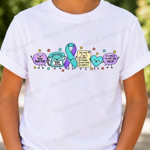 Könnte beinhalten: Ein weißes T-Shirt mit einer bunten Grafik, bestehend aus einer lila Sprechblase mit YOU MATTER, einem türkisfarbenen Telefon mit 988 LIFELINE, einer türkisen und lila Schleife, einer gelben Liste mit YOU ARE LOVED STRONG NOT ALONE WORTH IT und einem Herz.