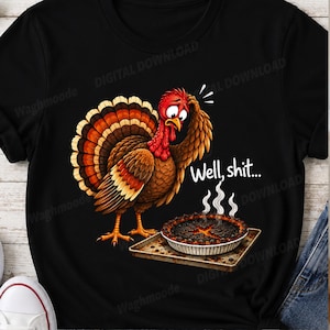 May include: A black t-shirt featuring a cartoon turkey with brown and orange feathers looking distressed while scratching its head. Next to the turkey is a burnt pie on a baking sheet with white steam rising. The text Well, shit... is printed in white.