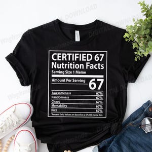 May include: Black t-shirt featuring a white graphic with the text "CERTIFIED 67 Nutrition Facts." The graphic resembles a nutrition label, listing percentages for various qualities. A casual black tee, suitable for everyday wear.