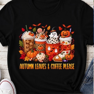 Könnte beinhalten: Ein schwarzes T-Shirt mit einer Grafik aus verschiedenen Kaffeetassen, Kürbissen, einem Geist und Herbstblättern. Das Design enthält den Text "AUTUMN LEAVES & COFFEE PLEASE" in orangefarbenen Buchstaben am unteren Rand, umgeben von herbstlichen Motiven.