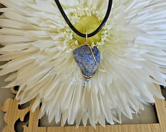 May include: A blue lapis lazuli stone pendant wrapped in gold wire, hanging from a black leather cord.
