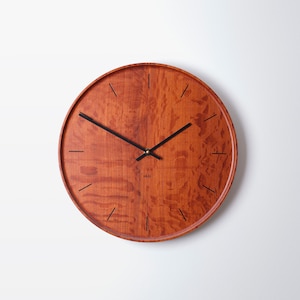 Peut inclure: Une horloge ronde en bois avec des aiguilles noires et un motif de grain de bois. Le cadran de l'horloge est de couleur brun clair avec des marques noires pour les heures et les minutes.