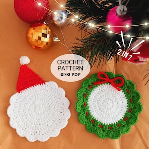 May include: Two crocheted Christmas ornaments, one a Santa Claus face with a red hat and the other a green wreath with a red bow. The ornaments are on a brown background with Christmas lights and ornaments.