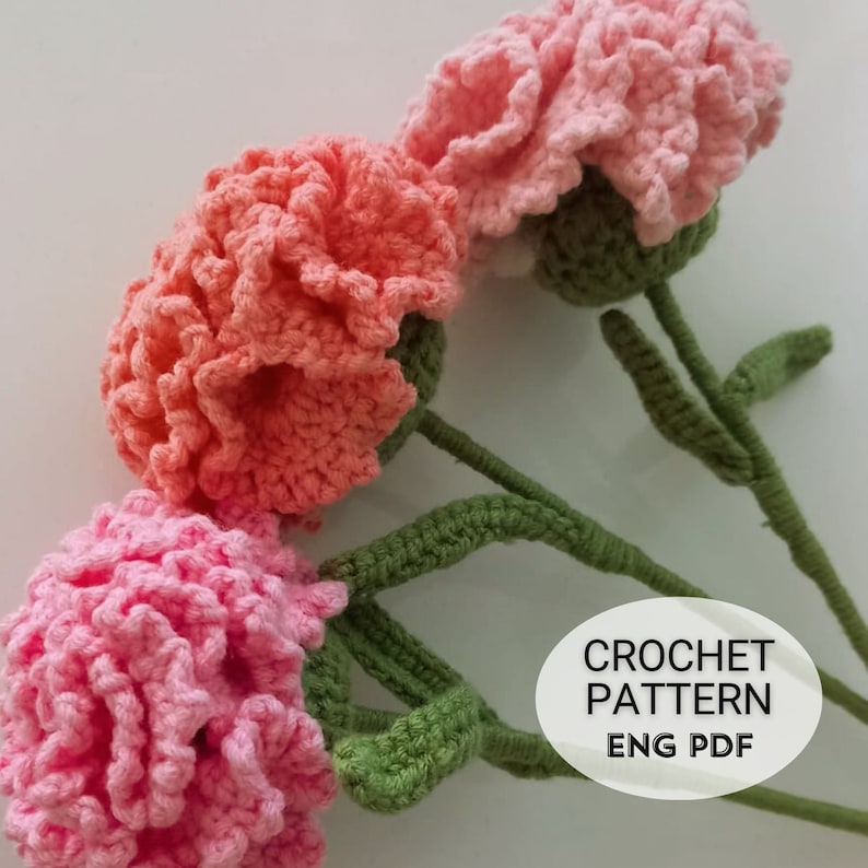 May include: Three crocheted carnations in pink and orange with green stems. The image includes the text "CROCHET PATTERN ENG PDF".