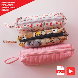 May include: Three quilted pencil cases in a stack. The top case has a white background with red cherries. The middle case has a tan background with animal illustrations. The bottom case is pink with a floral pattern. The text "FOR BEGINNERS PDF PATTERN VIDEO TUTORIAL ENGLISH" is in the top left corner.