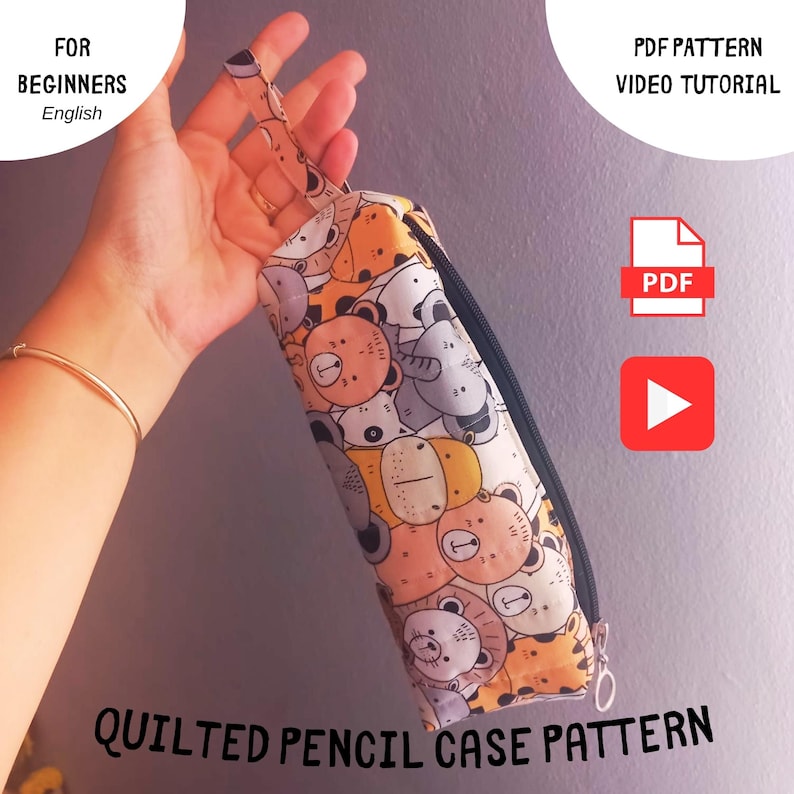 May include: A quilted pencil case pattern with a colorful animal print, held by a hand. The pencil case has a black zipper and a loop. Text on the image reads "For Beginners" and "Quilted Pencil Case Pattern."