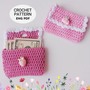 May include: Two pink crochet wallets with white trim and strawberry-shaped buttons. One wallet is open, revealing US currency. The image includes the text "CROCHET PATTERN ENG PDF".