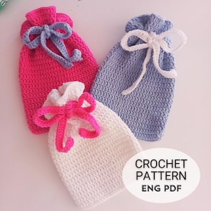 Puede incluir: Tres bolsas de cordón de ganchillo en rosa, blanco y azul con lazos de cinta a juego. Las bolsas están sobre una superficie blanca con el texto "CROCHET PATTERN ENG PDF".