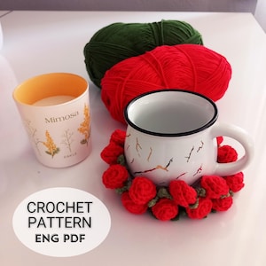 May include: A white enamel mug with a black rim and a crocheted red rose coaster. A candle holder with the word "Mimosa" and a floral design is next to the mug. Two balls of yarn, one red and one green, are in the background. The image also includes the text "CROCHET PATTERN ENG PDF".