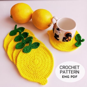 May include: Four crocheted lemon-shaped coasters in yellow with green leaves. The coasters are on a white surface with two whole lemons.