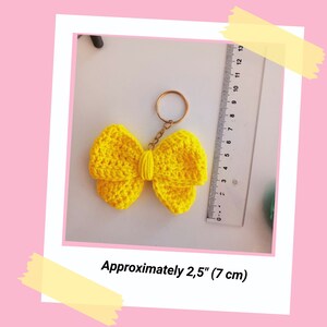 May include: A yellow crocheted bow keychain with a gold metal ring. The bow is approximately 2.5 inches (7 cm) wide.