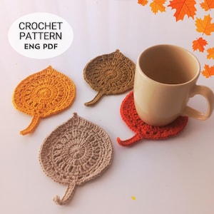 Puede incluir: Cuatro posavasos hechos a mano en forma de hoja de ganchillo en tonos naranja, marrón y beige. Una taza beige se encuentra sobre uno de los posavasos. La imagen incluye el texto "CROCHET PATTERN ENG PDF".