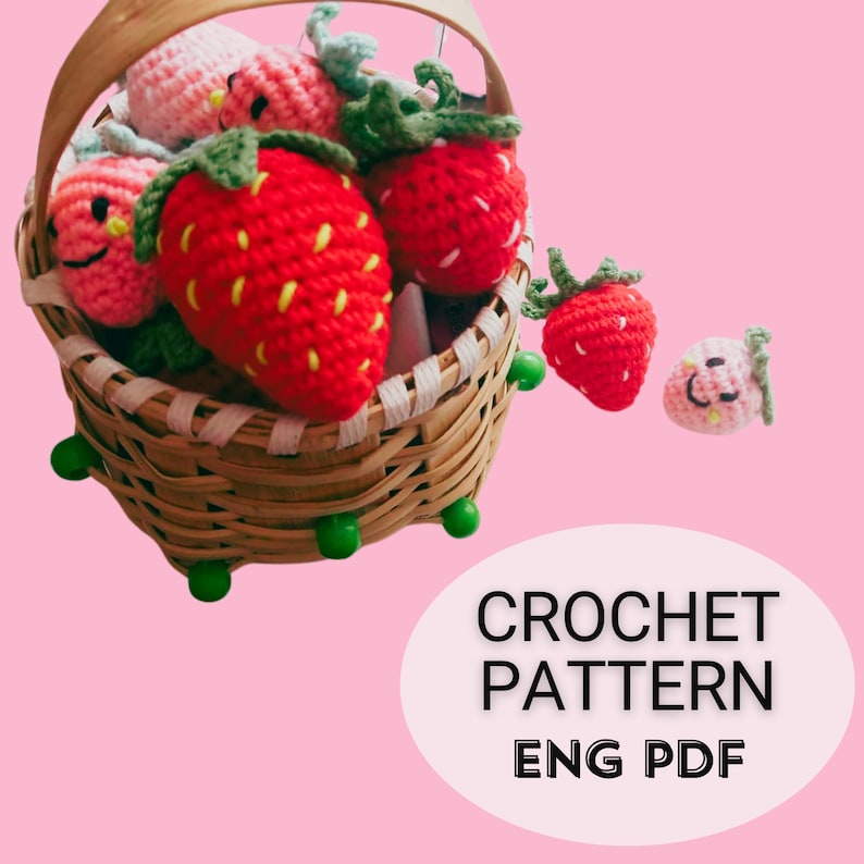 May include: A wicker basket containing multiple crocheted strawberries. The strawberries are red with green tops and yellow seed detailing. Some have smiling faces. The text "CROCHET PATTERN ENG PDF" is displayed on a pink background.